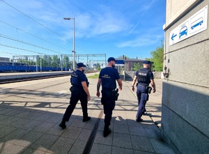 Na zdjęciu policjant oraz strażnicy ochrony kolei patrolują teren dworca kolejowego.