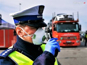 umundurowany policjant z maseczką na twarzy, trzymający w dłoni radiostację