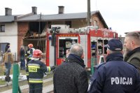 komendant burmistrz i naczelnik wydziału zarządzania kryzysowego spoglądają na miejsce tragedii. W tle zniszczony budynek i strażacy