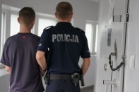 policjant trzyma za rękę podejrzanego. stoją w korytarzu policyjnego aresztu.