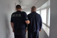 Policjant trzyma osobę zatrzymaną.