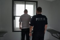 Zatrzymany mężczyzna przebywający w pomieszczeniu dla osób zatrzymanych rybnickiej komendy. Na zdjęciu widać również umundurowanego policjanta.