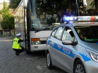 Policjant sprawdzający stan techniczny autokaru. Z przodu zdjęcia widać również oznakowany radiowóz.