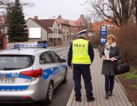 Mundurowy wręcza odblask mieszkance powiatu rybnickiego. Tuż obok policyjny radiowóz.