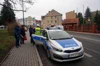 Grupa osób, której policjant wręcza opaski odblaskowe. Obok radiowóz.