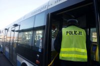 Umundurowany policjant stoi przed autobusem komunikacji miejskiej.
