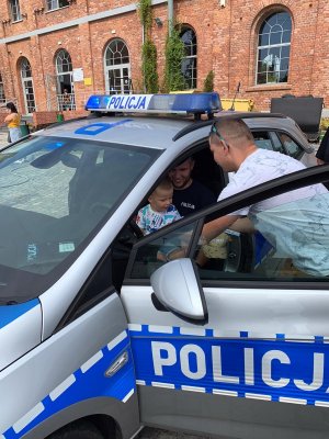 Policyjny radiowóz. Policjant trzyma na kolanach dziecko.