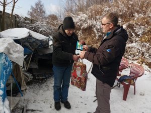 Streetworker wręcza bezdomnemu świąteczną paczkę.