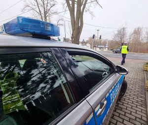 Oznakowany radiowóz, a w tle umundurowany policjant z Wydziału Ruchu Drogowego.