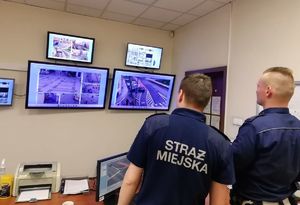 Policjant i strażnik miejski przeglądają monitoring miejski.