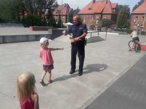 Policjant podczas akcji profilaktycznej rozdaje dzieciom ulotki ze wskazówkami dotyczącymi bezpieczeństwa.