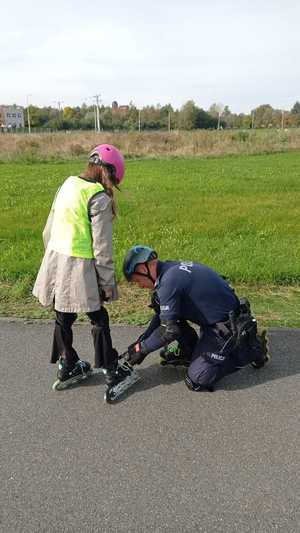 Policjant sprawdza dziewczynce, czy ma dobrze zapięte rolki. Działania „Bezpieczny sk8park &amp; pumptrack” z dzielnicowym.