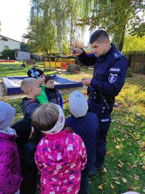 Policjant rozmawia z przedszkolakami na placu zabaw.