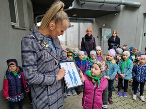 Pani przedszkolanka prezentuje obrazek, który przygotowały przedszkolaki dla Paana Komendanta.