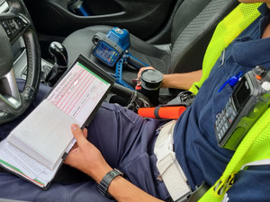 Policjant trzyma w ręku bloczek mandatowy.