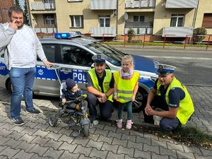 Policjanci i uczestnicy ruchu drogowego przy radiowozie.