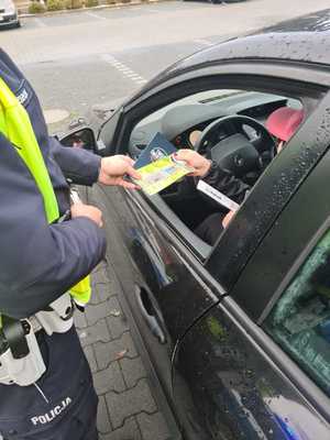 Na zdjęciu policjant wręcza ulotki i odblask kierującej.