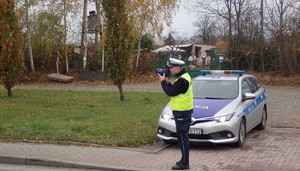 Na zdjęciu policjant stoi przed radiowozem i dokonuje pomiaru prędkości.