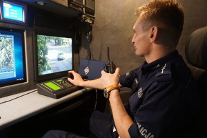 Na zdjęciu policjant ruchu drogowego obserwujący w oku kamery przejście dla pieszych.