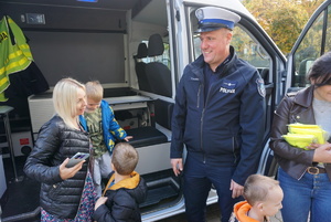 Na zdjęciu policjant z ruchu drogowego opowiada dzieciom o bezpiecznych zrachowaniach na drodze.