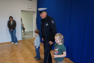 Na zdjęciu policjant uczy dzieci, jak bezpiecznie przejść przejście dla pieszych.