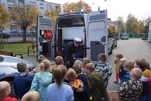 Na zdjęciu policjant prezentuje dzieciom policyjne akcesoria.