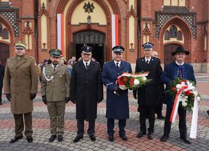 Na zdjęciu Szef rybnickich policjantów oraz przedstawiciele innych służb mundurowych. W tle kościół.