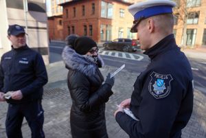 Na zdjęciu dwóch umundurowanych policjantów rozdających opaski odblaskowe.