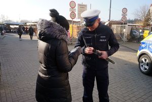 Na zdjęciu policjant wręcza seniorce opaskę odblaskową.