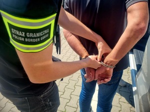 Na zdjęciu funkcjonariusz Straży Granicznej zakłada zatrzymanemu kajdanki na ręce trzymane z tyłu.