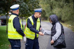 Na zdjęciu umundurowani policjanci rozdają mieszkańcom odblaski.
