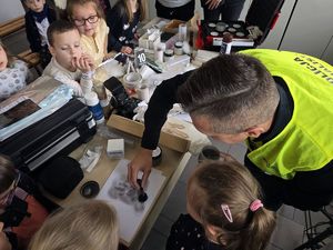 Na zdjęciu technik kryminalistyki pokazuje dzieciom, jak zabezpieczyć ślady kryminalistyczne.