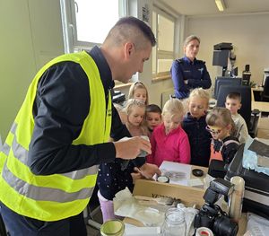 Na zdjęciu technik kryminalistyki prezentuje dzieciom, jak zabezpieczyć ślady.